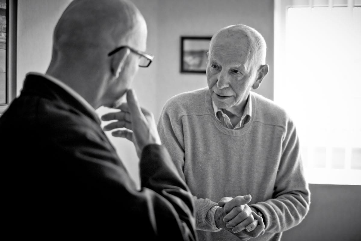 A black and white over the shoulder shot, showing David Lancaster talking to John Surtees.